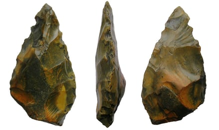 A thick butted, pointed handaxe. The implement measures 132mm high by 65.6mm wide and 28mm thick (5.2" x 2.58" x 1.1"). The base of the tool is only roughly shaped, with some of the natural surface of the flint having been left on. Traces of the natural flint surface can also be seen on one side of the body. The object tapers gradually to a point. Broad flake removal scars can be seen on both faces and there is some re-touching of the edges and point. The surface of the flint is heavily weathered and is generally light yellow to deep orange in colour. The object weighs 364.7g.